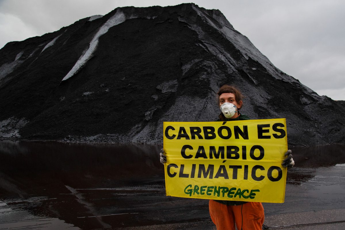 Una activista de Greenpeace delante de una montaña de carbón sujeta un cartel que dice Carbón es cambio climático