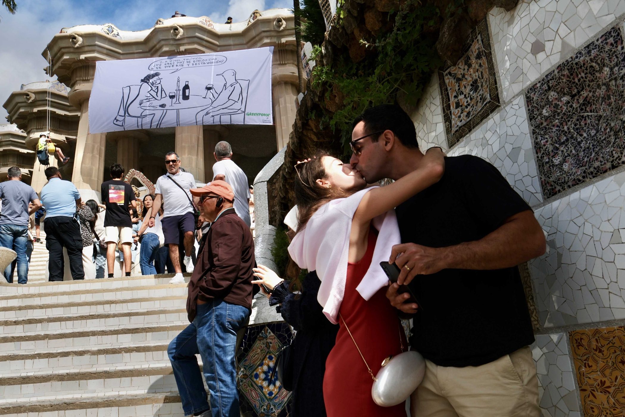 Dos personas se besan en el Park Güell de Barcelona durante le día del medio ambiente. Al fondo se ve una viñeta gigante de Flavita Banana.