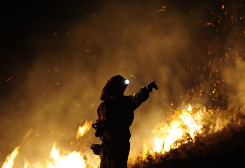 Un bombero da indicaciones mientras las llamas del fuego devoran un bosque tras él.
